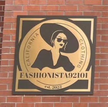 Fashionista92101 logo on brick wall featuring stylized woman in hat and sunglasses, established 2023